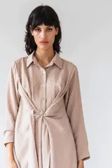 Camisa manga larga color beige con textura plumetie, abotonada en el pecho y lazo regulable que permite múltiples usos.