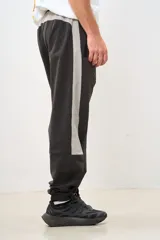 Pantalón de jogging gris oscuro con banda lateral gris claro, cintura elástica con cordón ajustable, bolsillos laterales con cierre y puños elásticos.