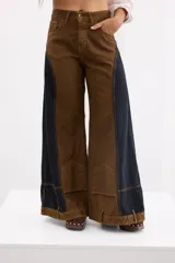 Pantalón de jean estilo wide leg con diseño bicolor en tonos marrón y negro. Presenta paneles laterales oscuros, costuras a la vista en color ocre y bolsillos frontales tipo parche en la parte inferior de las piernas.