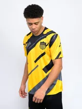 Remera de entrenamiento Fynar del Club Atlético Peñarol, color negro con estampado geométrico en amarillo y gris. Presenta cuello redondo, mangas cortas y el escudo del club en el pecho.