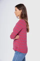 Remera de manga larga con cuello redondo, confeccionada en tejido rayado horizontal en tonos rojo y azul, con detalle de pin metálico con logo en la parte frontal.