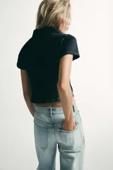 Camisa de denim entallada con cuello solapa, escote en pico y manga corta. Presenta costuras marcadas y cierre frontal con botones.