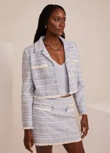 Chaqueta corta de tweed celeste con detalles en blanco y dorado, de corte sastre, con solapas de pico, cierre frontal con botones, bolsillos delanteros y terminaciones con flecos.