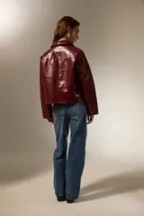 Chaqueta de eco-cuero negro con acabado brillante, cuello camisero, cierre frontal con botones y mangas largas.