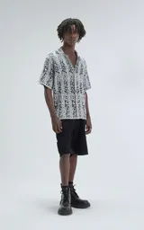 Camisa de manga corta, tejida de punto abierto (símil crochet), color blanco y negro con estampado paisley. Tiene cuello tipo solapa y calce oversize.