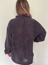 Buzo negro de pana con cierre metálico en el cuello, corte holgado y mangas largas con puños elásticos.