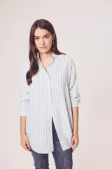 Camisa oversize celeste y blanca a rayas verticales, de mangas largas con puños abotonados y cuello camisero.
