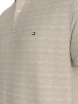 Chomba de corte regular color beige claro, con cuello tipo chomba, cartera de dos botones y logo de Tommy Hilfiger bordado en el pecho. Diseño de rayas en el interior del cuello.