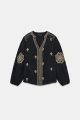 Camisa negra de manga larga con cuello redondo y escote en V, adornada con bordados florales en contraste en tonos beige y marrón a lo largo de la abertura frontal, hombros y mangas.