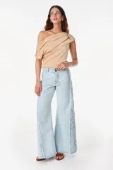 Blusa asimétrica color beige de poliéster con spandex, con diseño drapeado envolvente que deja un hombro al descubierto y manga corta caída del otro lado.