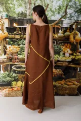 Vestido largo de lino marrón con cuello semi-bote, sin mangas y aberturas laterales en el bajo. Cuenta con detalles de líneas en color amarillo a contratono que recorren la prenda de forma diagonal.