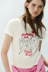 Camiseta blanca de algodón con cuello redondo, manga corta y calce regular. Presenta un estampado frontal ilustrado con conejos, corazones, estrellas y el texto "Kindness for every kind".