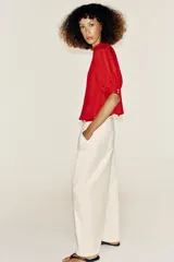 Blusa blanca de cuello alto con detalles de puntilla, manga corta abullonada y cierre posterior con botón.