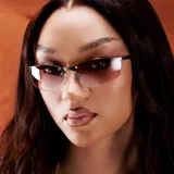 Lentes de sol con diseño envolvente, montura de acero inoxidable en color gris oscuro y lentes de nylon en tono marrón degradado. Presentan una estructura superior metálica con detalles de remaches y patillas con terminaciones en acetato.