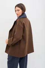 Tapado de paño de lana color marrón con silueta oversize y hombros caídos. Presenta doble abotonadura frontal, solapas amplias con detalle en contraste azul, y mangas con ajuste en los puños.