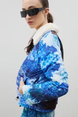 Campera con estampado de bosque en tonos azules, cuello de sherpa en color crema y cierre frontal con cremallera. Cuenta con elástico ajustable en la cintura.