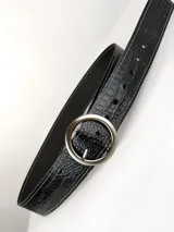 Cinto de cuero negro con textura de reptil, hebilla circular metálica en tono bronce envejecido y detalles de remaches metálicos.