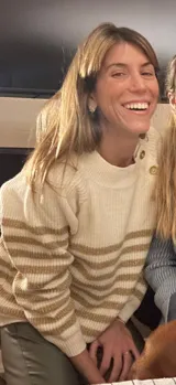 Sweater de punto en color crema con rayas horizontales en tono dorado. Presenta un diseño de cuello redondo con una solapa lateral decorada con botones metálicos dorados y corte holgado.