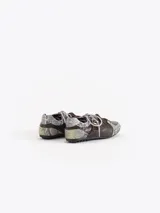 Zapatillas de cuero vacuno en color beige, con recortes de gamuza en la puntera y talón, doble cordón en tonos gris y marrón, hebilla lateral y dije colgante en la cordonera. Suela plana de goma.
