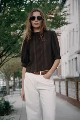 Blusa blanca de cuello alto con detalles de puntilla, manga corta abullonada y cierre posterior con botón.