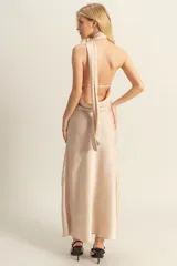 Vestido largo de satén color beige, con escote halter, espalda descubierta y tajo lateral en la falda.