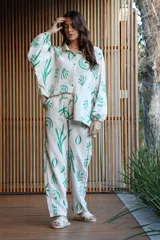 Conjunto de dos piezas compuesto por camisa de corte oversize con mangas largas y pantalón de corte recto, ambos confeccionados en tela color crudo con estampado botánico en color verde.