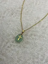 Collar con cadena dorada y dije de piedra natural pulida con cruz dorada incrustada. Disponible en tres colores: rosa, lila y blanco.