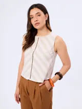 Blusa sin mangas con cuello redondo, de corte recto y diseño a rayas diagonales en tonos beige y blanco, con detalle de abertura central vertical decorada con costura ajurada.