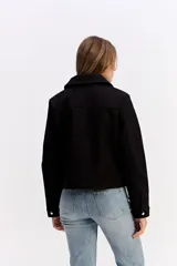 Campera corta de paño color negro, con cierre frontal metálico, cuello camisero y bolsillos frontales con solapa y botón metálico.