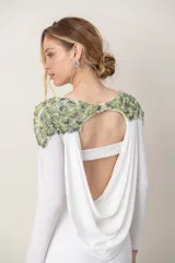 Vestido largo blanco de manga larga, con escote redondo al frente, espalda baja descubierta y detalles de bordado de piedras y pedrería en tonos verdes sobre los hombros.