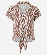Blusa de manga corta confeccionada en viscosa, con cuello camisero, cierre frontal con botones y detalle de lazo para anudar en el bajo. Presenta un estampado híbrido entre follaje y animal print de cebra en tonos marrón y blanco.