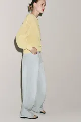Chaqueta de punto rústico color amarillo claro, con cuello redondo, manga larga y cierre frontal con botones nacarados.