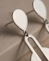 Caravanas colgantes de acero con diseño geométrico compuesto por una pieza superior en forma de gota y una pieza inferior circular con una abertura ovalada central.