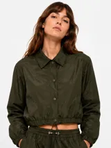 Campera corta verde militar de nylon, con cuello camisero, cierre frontal con botones a presión y elástico ajustable en el ruedo.
