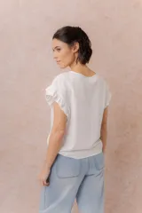 Blusa blanca con escote redondo y mangas cortas con volados. Corte relajado y caída suave.