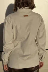 Camisa de pana color verde oliva, con cuello alto con volados, cierre frontal de botones y mangas largas con puños.