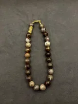 Collar de cuentas de piedras naturales en tonos tierra, con detalles de tubos dorados en los laterales.