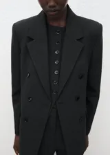 Chaqueta de corte recto y estilo sastre, confeccionada en tejido de poliéster y viscosa. Presenta cuello con solapas de muesca, cierre frontal de doble botonadura y mangas largas con puños abotonados. Incluye dos bolsillos laterales con solapa y abertura posterior en el bajo.