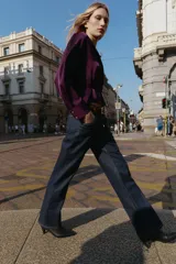 Camisa satinada de color violeta oscuro, con cuello solapa, escote en pico y manga larga. Presenta un detalle de cinturón fino ajustable a tono en la cintura y cierre frontal con botones.