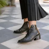 Botín de cuero vacuno color marrón oscuro, con taco de madera foliado en cuero de 5cm de altura, cierre lateral interno y horma de punta fina.