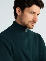 Sweater de punto color verde oscuro, con cuello alto y cierre frontal parcial, de manga larga y puños acanalados.