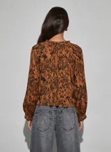 Camisa de manga larga con estampado animal print, cuello redondo con volados y cordón ajustable, y cierre frontal con botones.