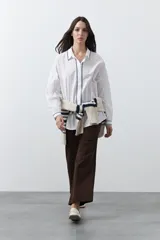 Camisa blanca de manga larga con detalles bordados en contraste a lo largo de la botonadura, el cuello y los puños. Presenta una silueta relajada y un diseño clásico con un toque artesanal.