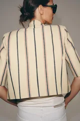 Blazer cropped ZW Collection confeccionada en mezcla de algodón, con diseño a rayas verticales en tonos azul y rojo sobre base beige. Presenta cuello redondo, manga corta, forro interior a tono y cierre frontal con un botón.