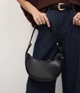 Bolso baguette en formato media luna, con correa de hombro ajustable mediante detalles metálicos y cierre superior por cremallera. Diseño minimalista con acabado liso.