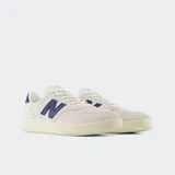 Championes urbanos New Balance modelo CT500, color blanco hueso con detalles en azul marino, confeccionados en gamuza y cuero, con logo "N" característico en los laterales y suela de goma.