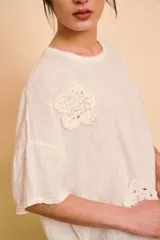 Blusa holgada color beige con mangas cortas y cuello redondo. Presenta apliques bordados con detalles de perlas y lentejuelas en el frente.