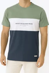 Remera de manga corta con diseño de bloques de color en tonos verde, blanco y azul marino. Presenta una estampa frontal con el texto 'LEGACY ESTABLISHED BRAND' y un pequeño parche de marca en el ruedo inferior.