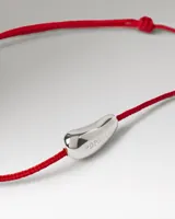 Pulsera de cordón rojo con un dije central plateado de diseño orgánico y grabado de la marca.