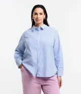 Camisa de corte clásico y largo, confeccionada en tejido anarruga con estampado de rayas verticales en tonos azul y blanco. Presenta cuello inglés, cierre frontal abotonado y mangas largas con puños.